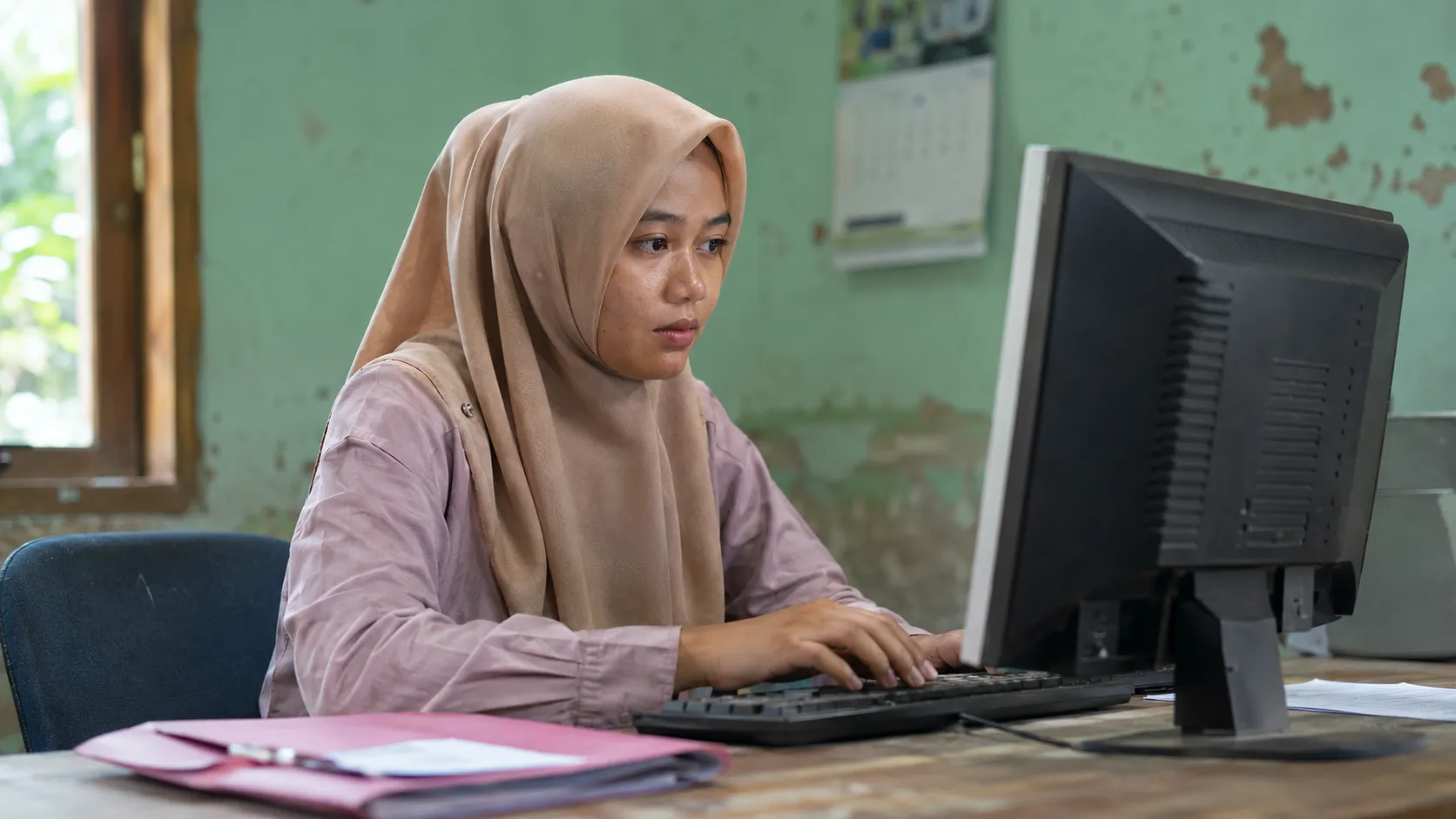 A local Indonesian female village worker in a simple hijab operating a modest computer dashboard to track supply chain metrics